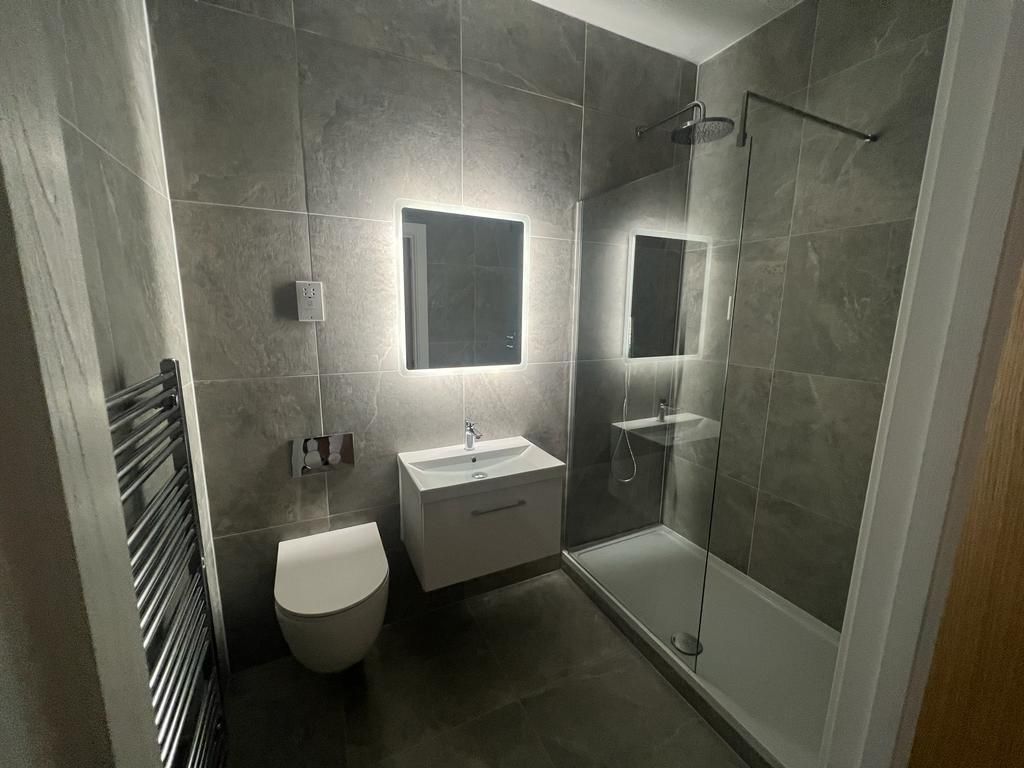 Modern bathroom with gray tile, white fixtures, and backlit mirror.