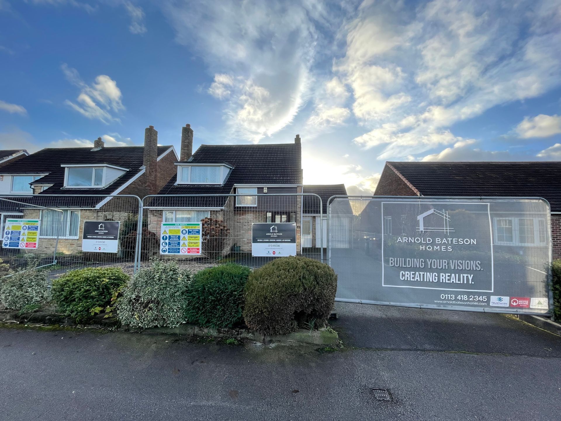 Houses under construction, fenced off, with a cloudy sky above. A banner advertises Arnold Bateman Homes.