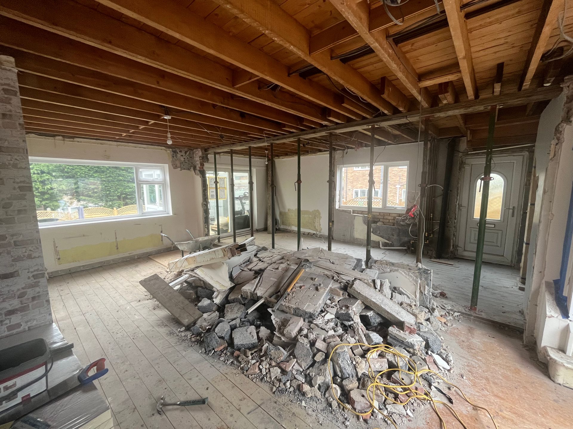Room under construction, debris pile on wooden floor. Exposed ceiling beams and support poles.