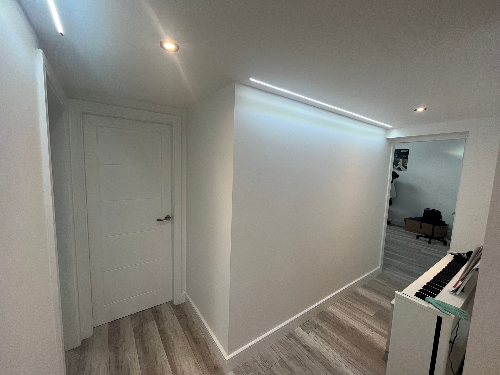 White hallway with a closed door on the left, a long wall, and a room visible at the end.