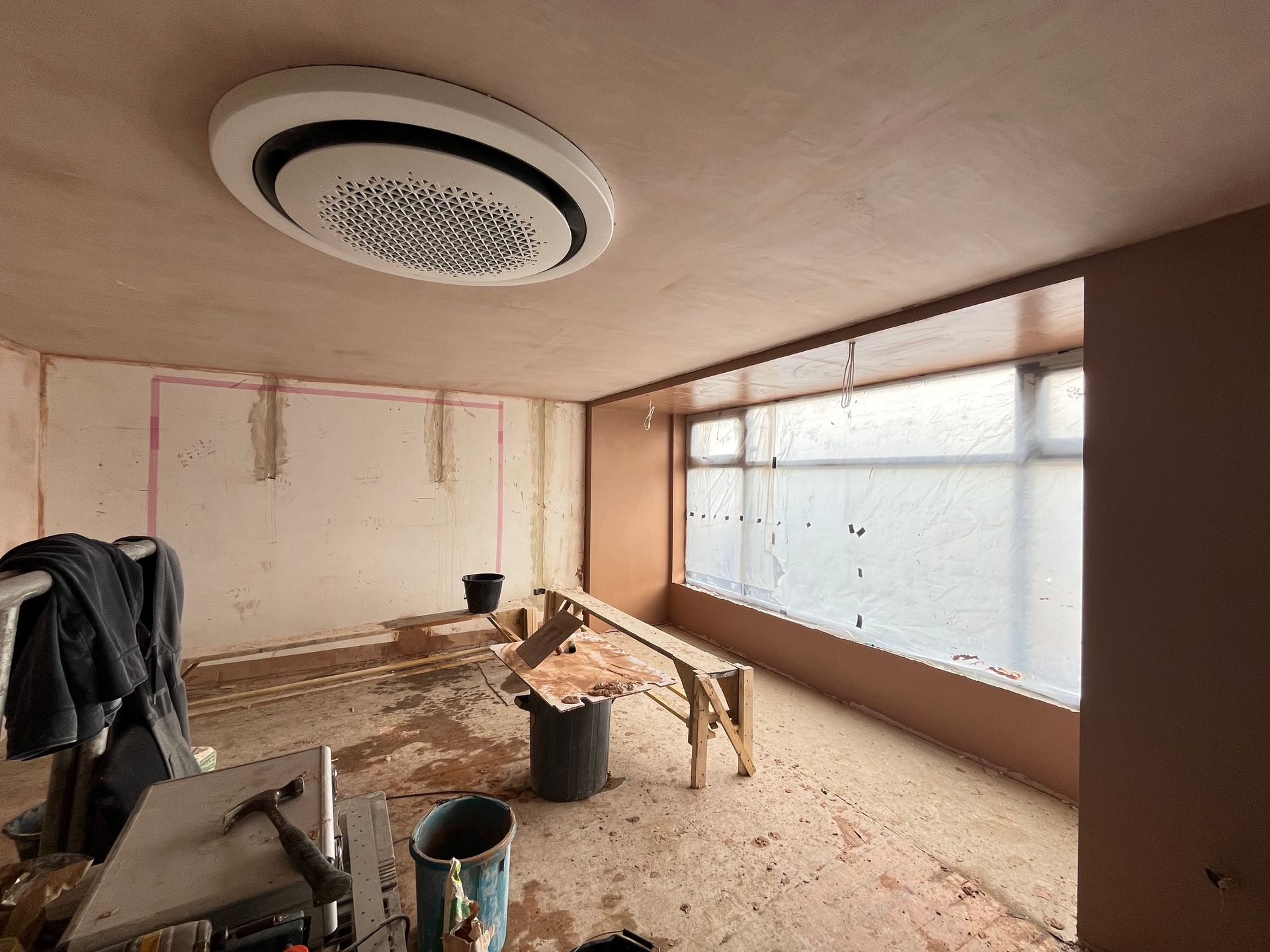 Room under construction with air conditioning unit, bare walls, covered window.