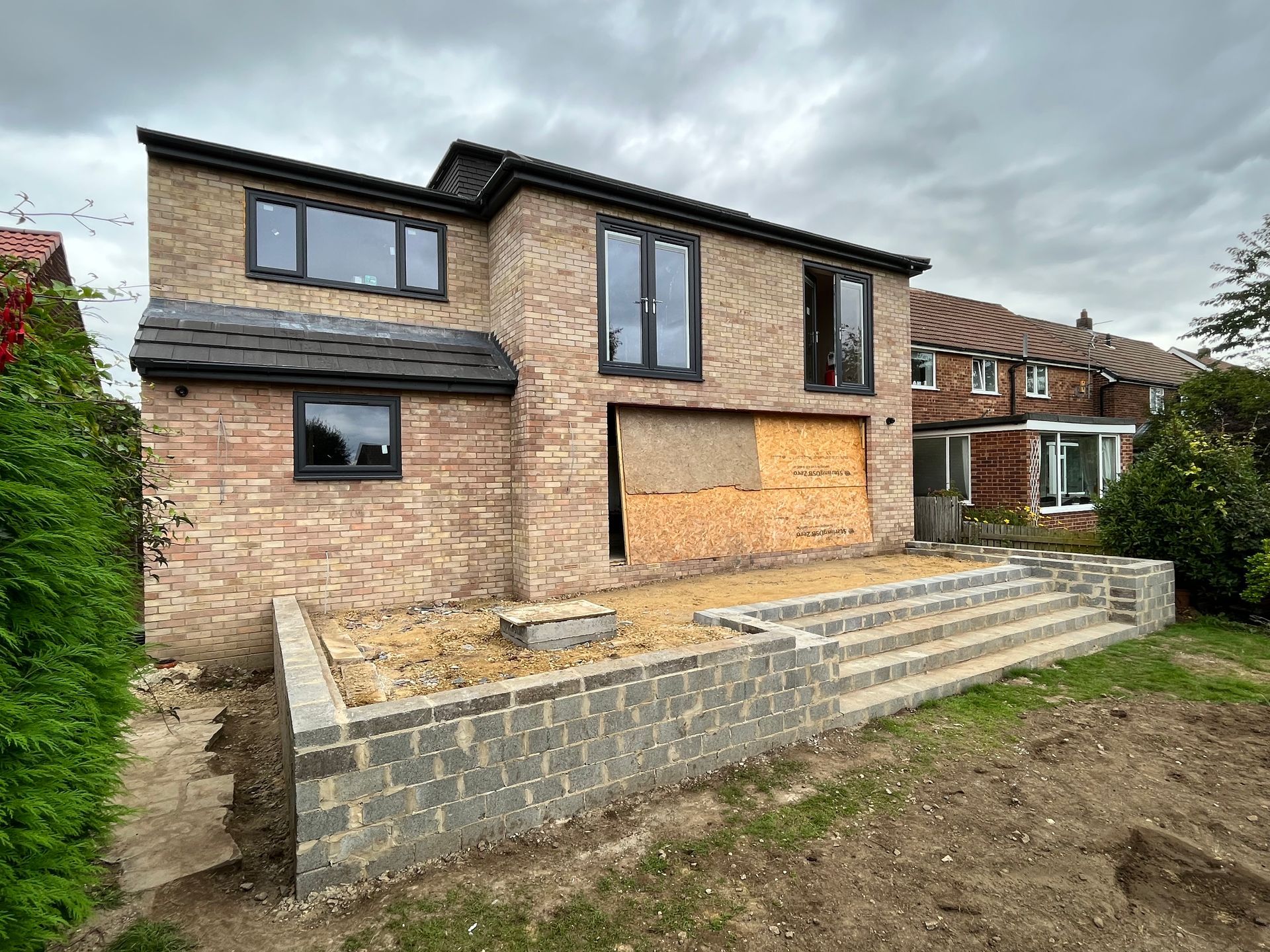 Brick house under construction with a new patio and steps, cloudy sky.