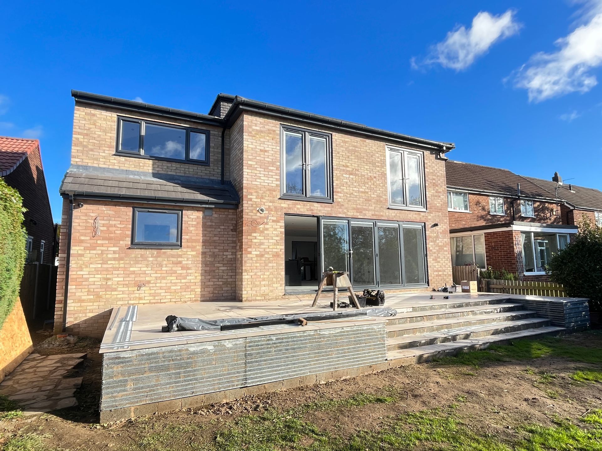 Two-story brick house with large windows and a patio under construction on a sunny day.