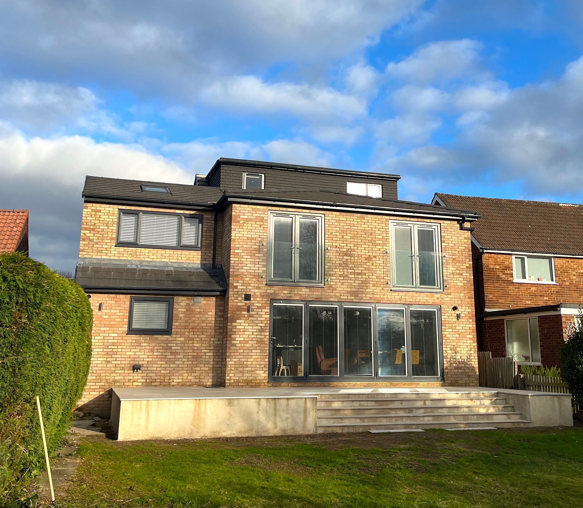 Brick house with multiple windows and a large patio, set against a cloudy blue sky.