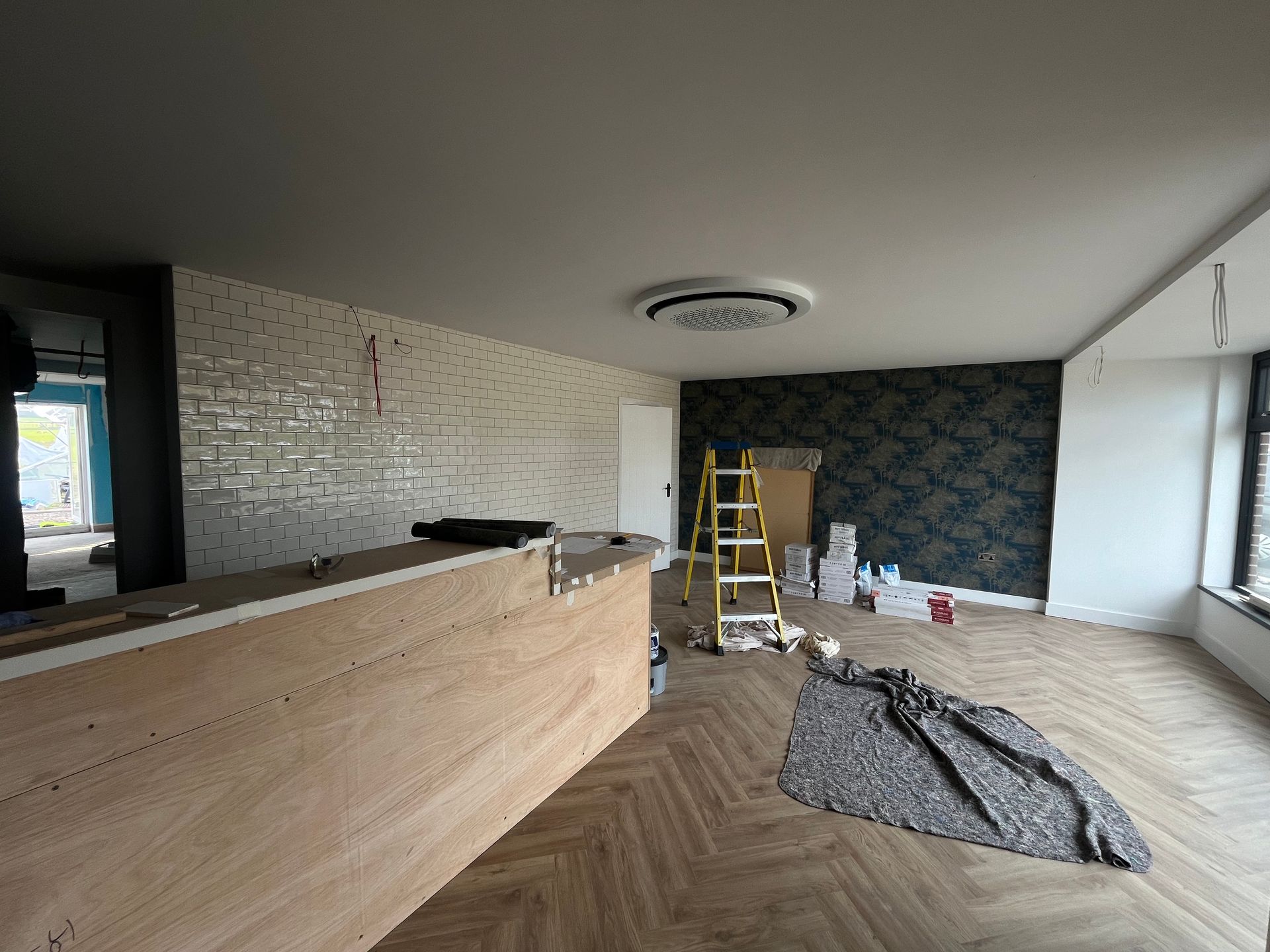 Interior of a room under renovation with a wood floor, brick-like wall, and a dark patterned wall.