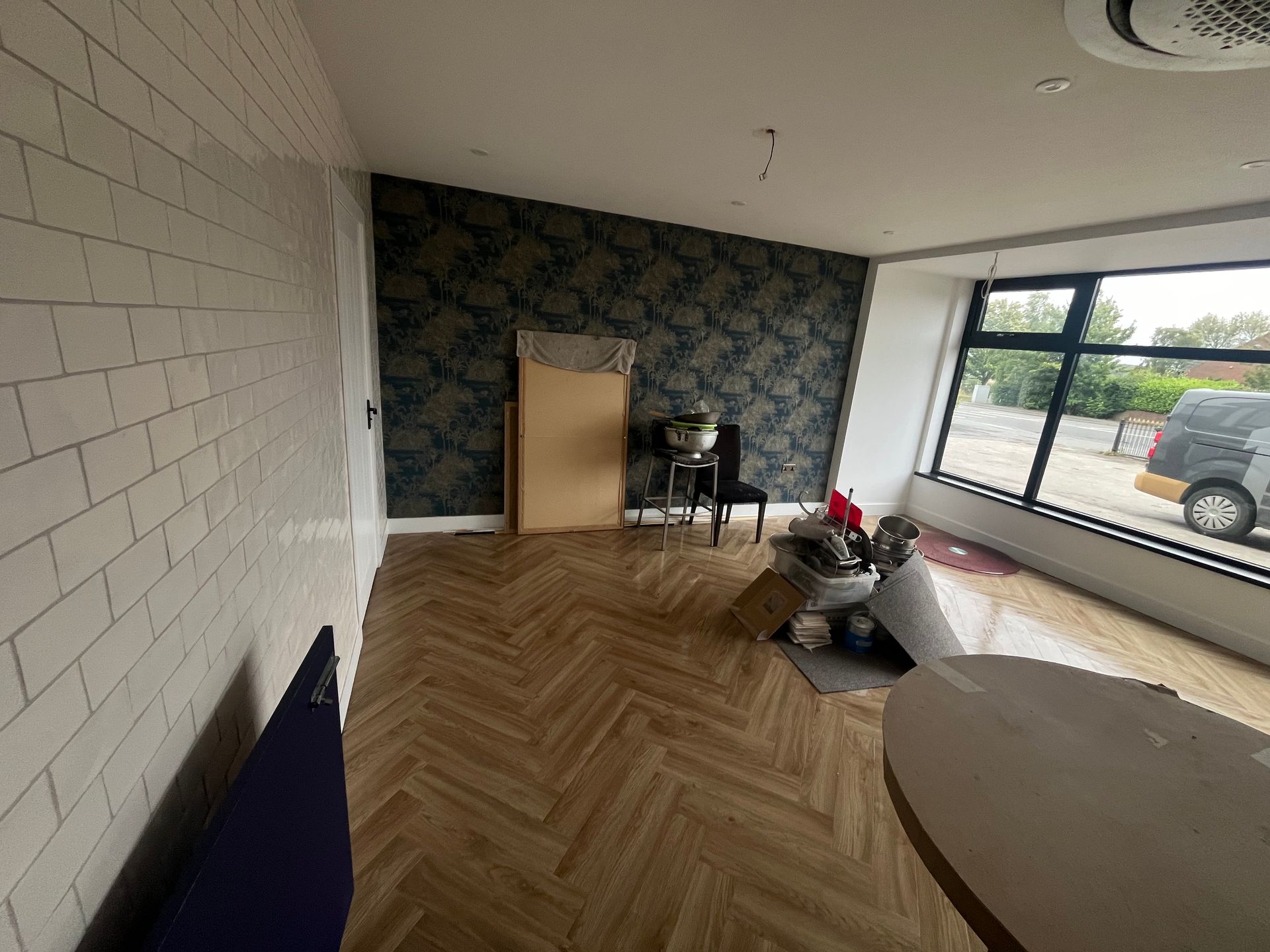Empty room with wood floor, white brick wall, dark floral wallpaper, and large window.