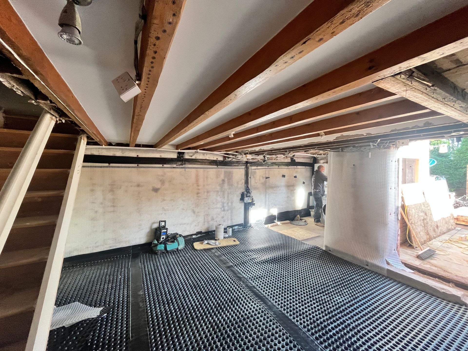 Basement undergoing renovation. Exposed ceiling beams, black radiant floor, and partially finished walls.