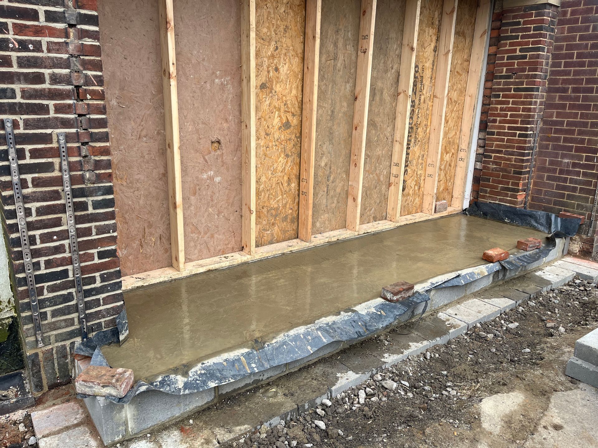 Construction site. Concrete poured inside a frame, brickwork visible on either side.