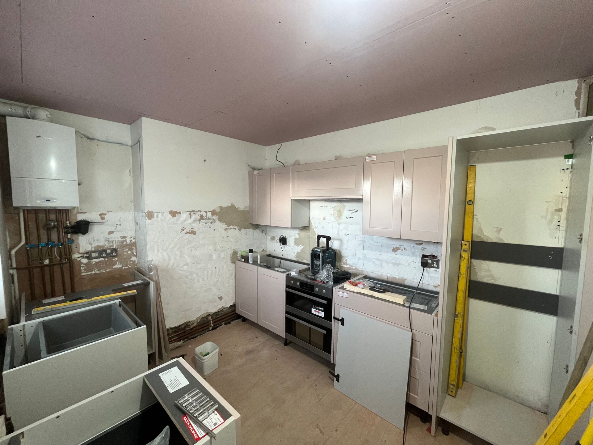 Kitchen under renovation; cabinets installed, walls stripped, water heater, appliances.