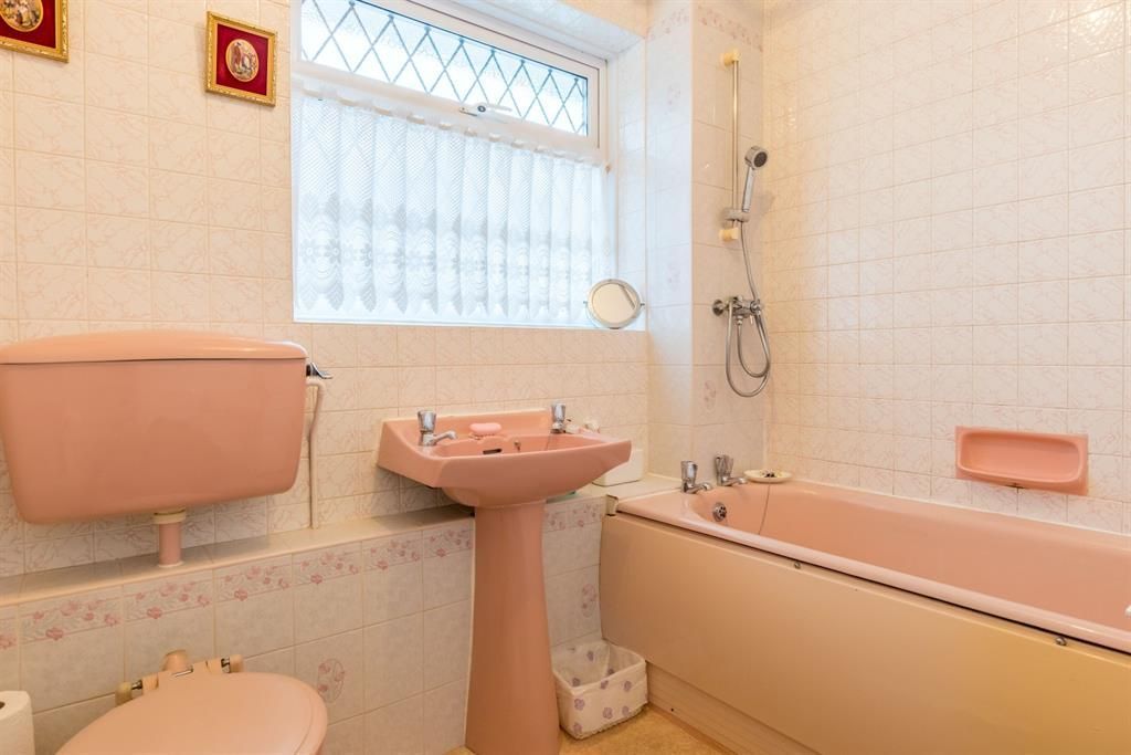 Pink bathroom with toilet, sink, bathtub, and window.