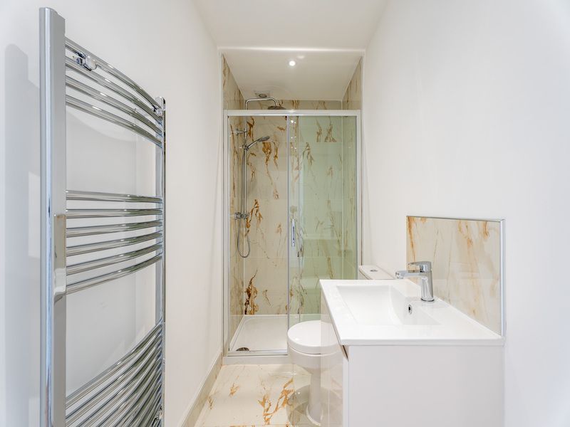 Small, white bathroom with marble-look shower and vanity. Chrome towel rack on left.