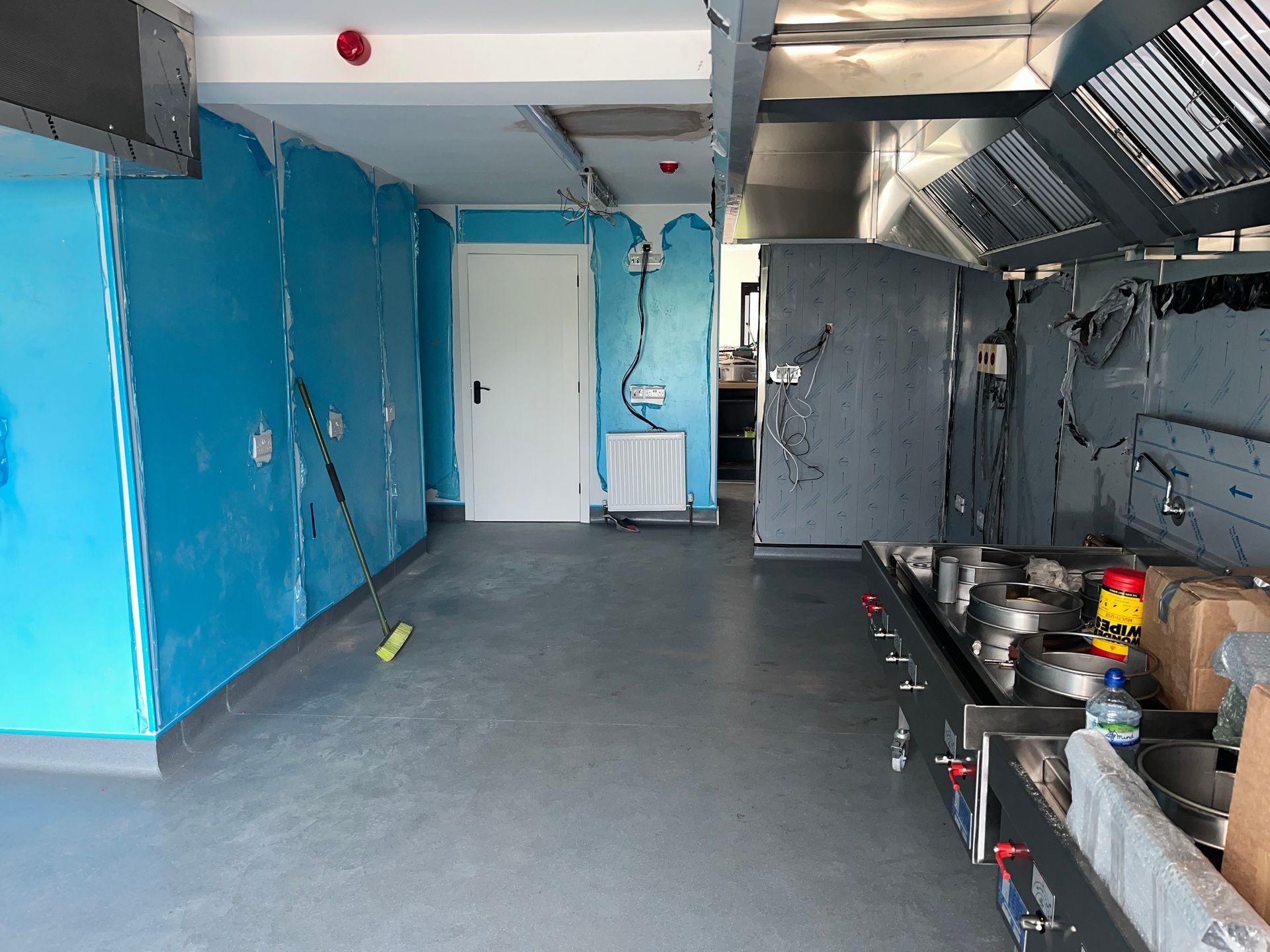 Empty commercial kitchen with blue walls, stainless steel appliances, and gray floor.