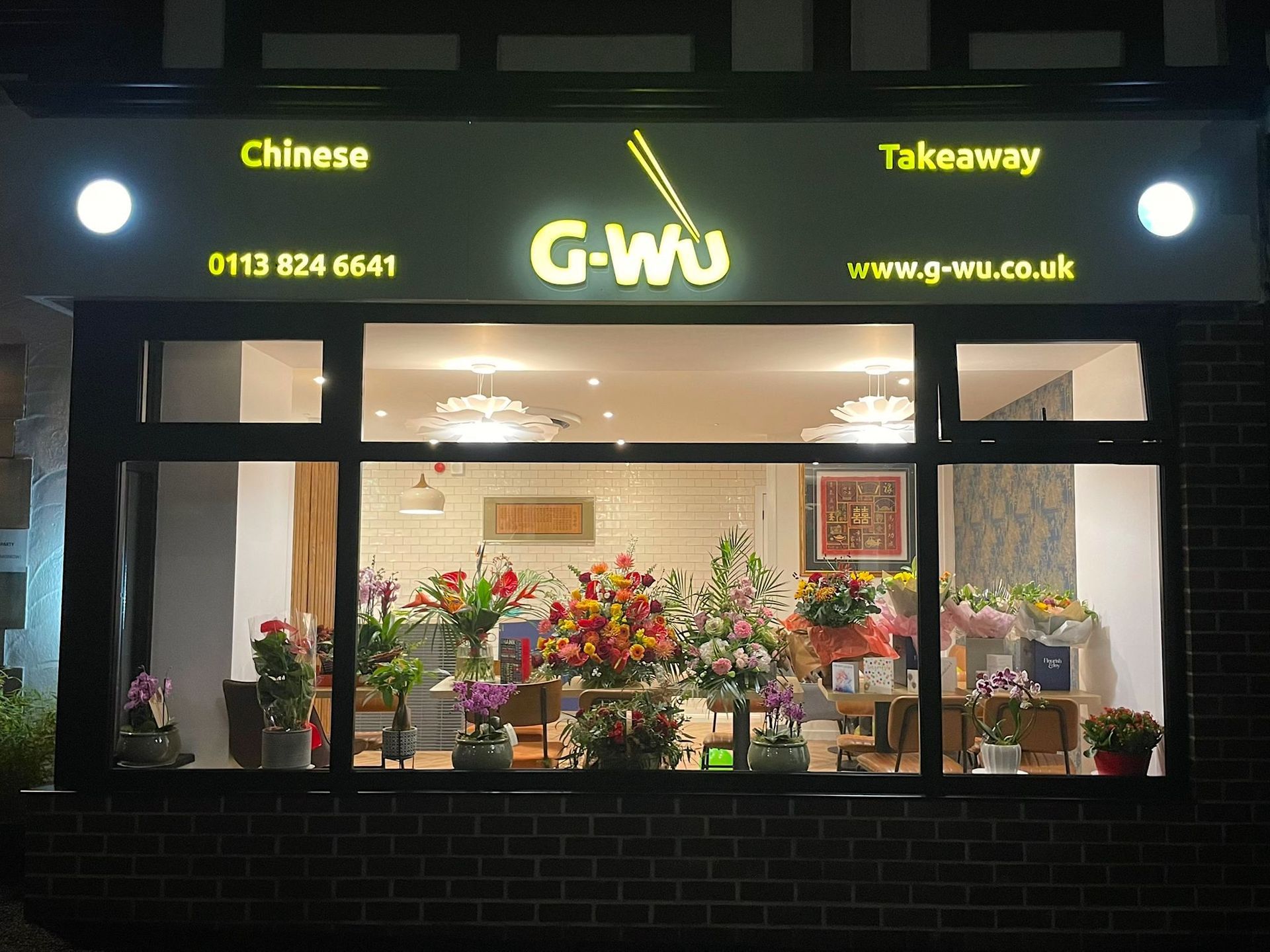 G-Wu Chinese Takeaway storefront at night, with window display of flowers and glowing sign.