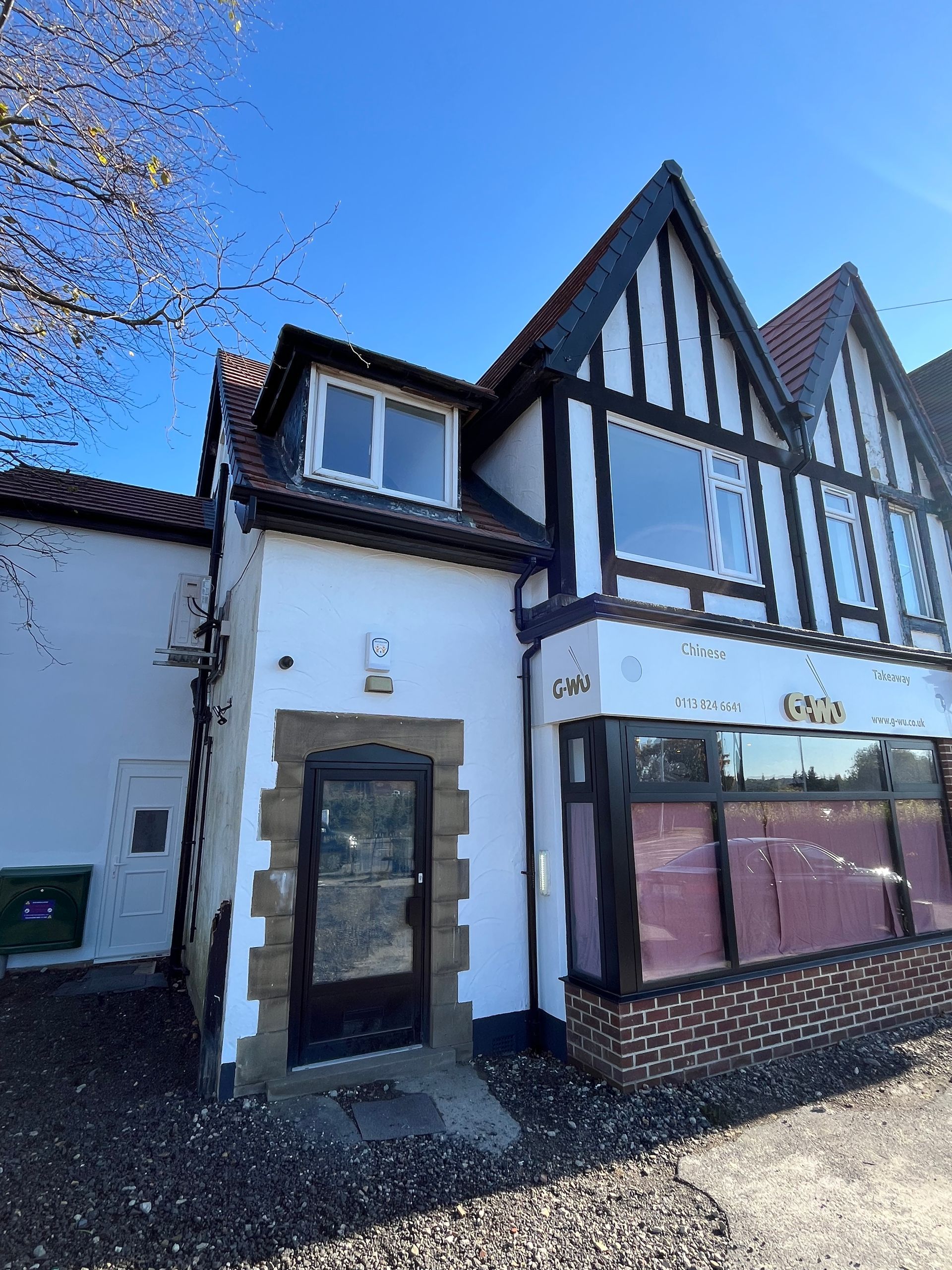 Tudor-style building with black trim, white walls, and a brick storefront under a clear blue sky.