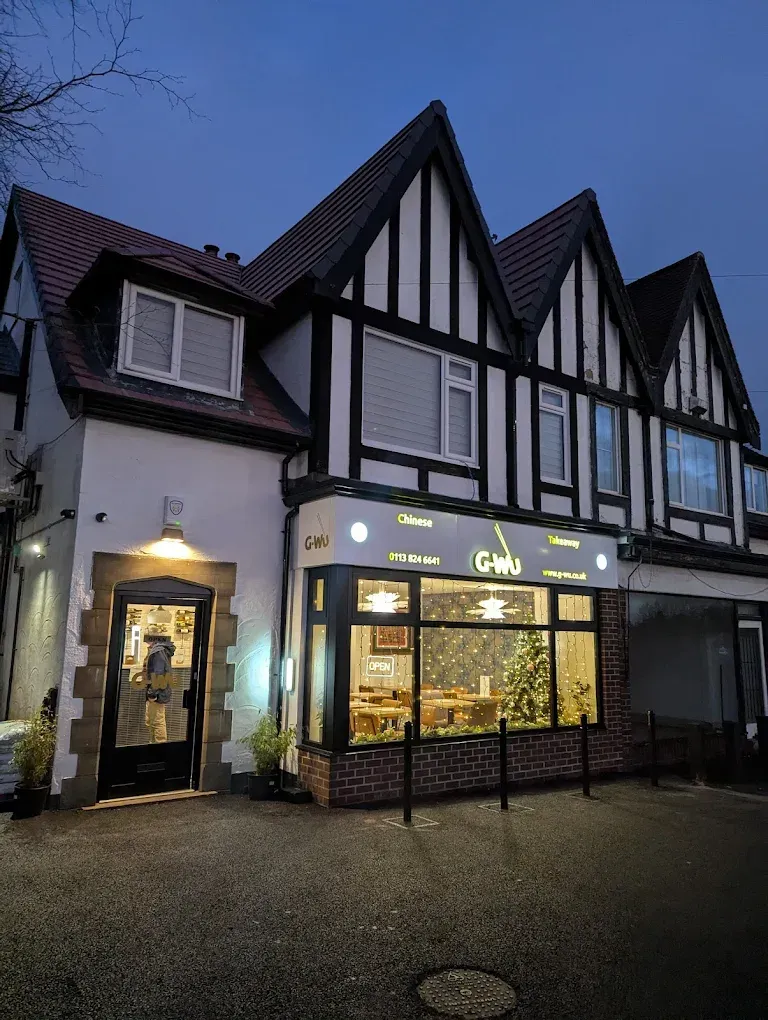 Restaurant exterior with illuminated sign, featuring white and black Tudor-style facade, at dusk.