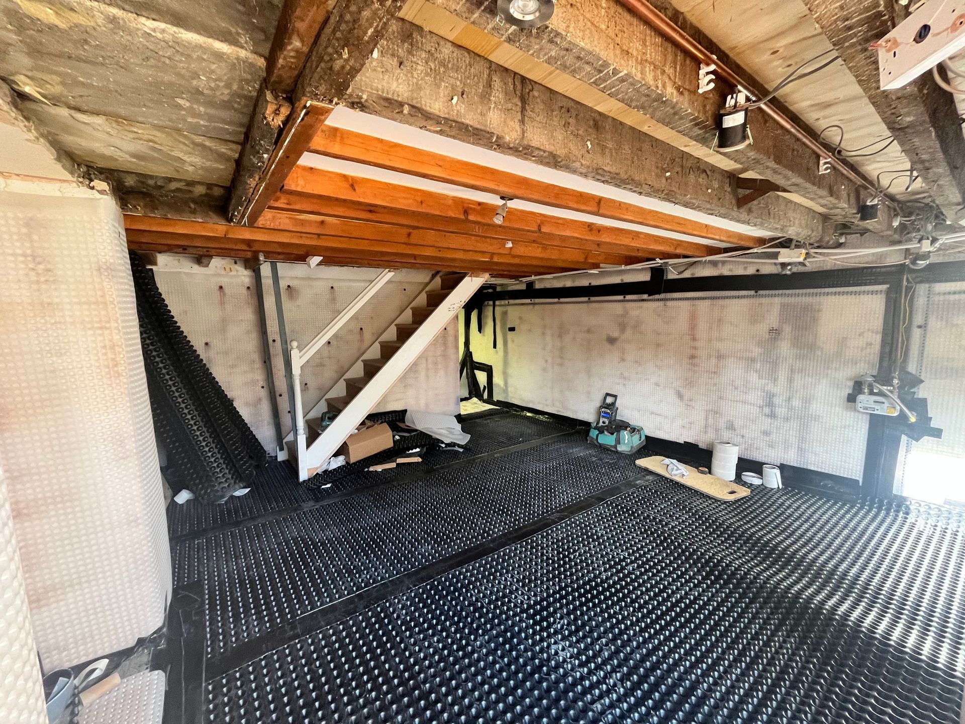Interior of a basement or garage under construction, showing black dimpled drainage membrane on the floor.