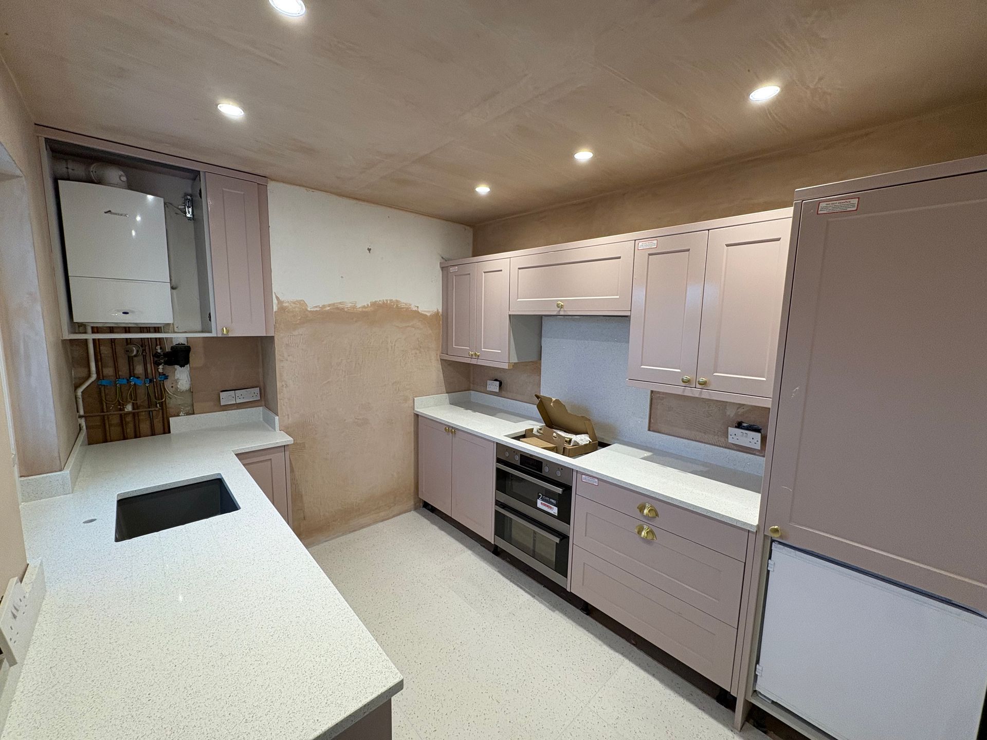 Newly renovated kitchen with pale pink cabinets, white countertops, and recessed lighting.