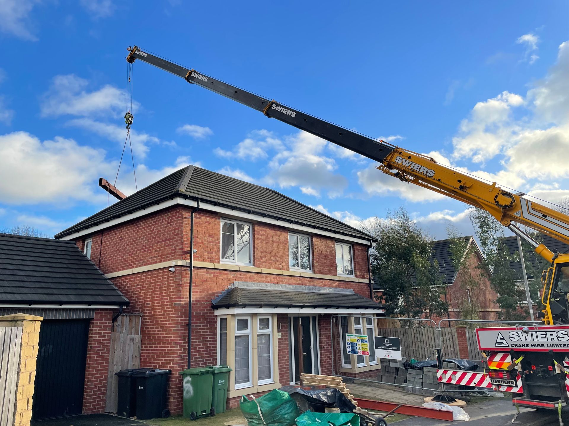 Crane removing roofing from a two-story brick house on a cloudy day.