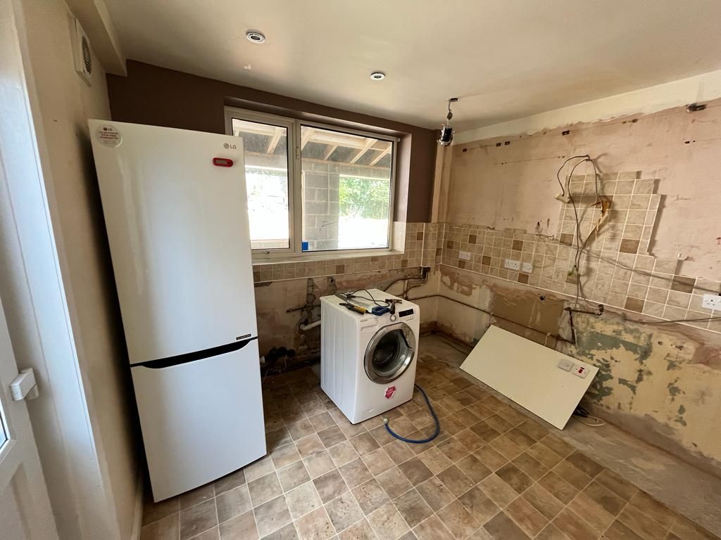 Kitchen under renovation with fridge, washing machine, and exposed walls.