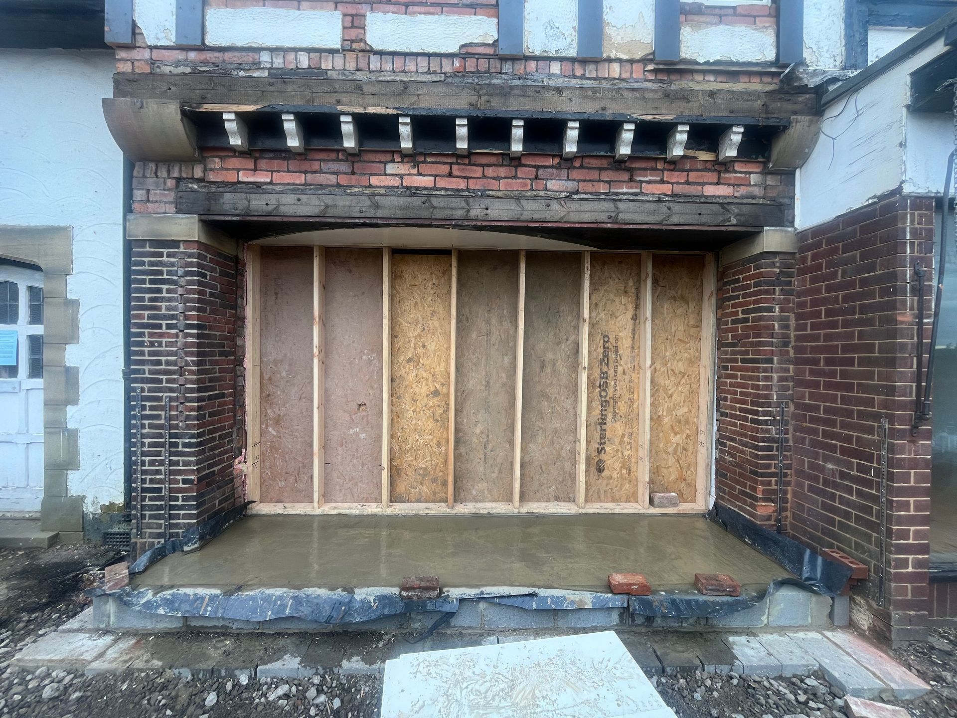 Exterior of building undergoing renovation; brick and wood facade with new plywood wall.