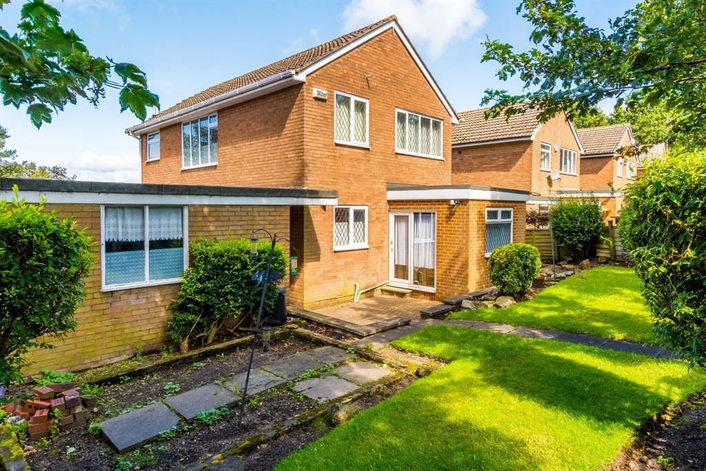 Two-story brick house with a garden and patio. Green grass, bushes, and a clear sky.