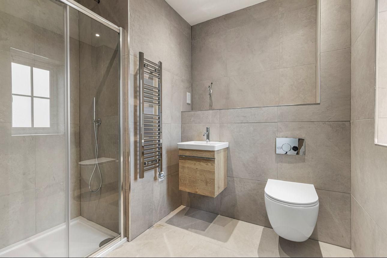 Modern gray bathroom with a shower, toilet, sink, and towel warmer.