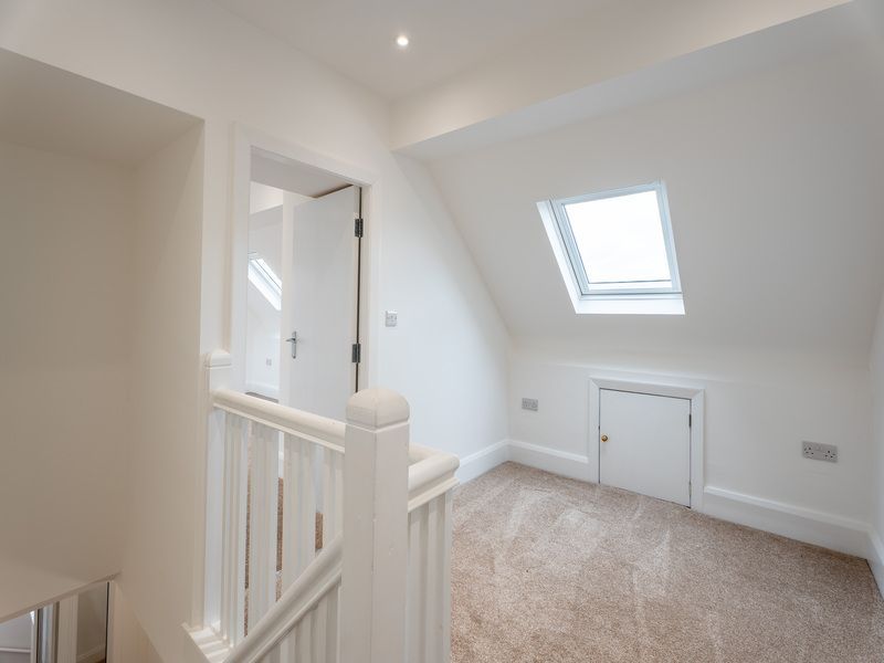 Attic interior with staircase, angled ceiling, skylight, small door, and beige carpet.