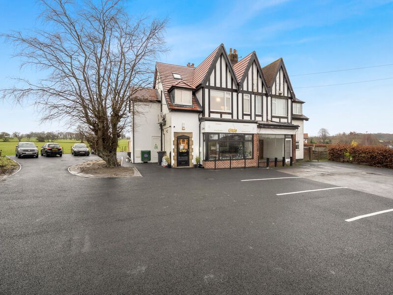 A two-story building with black and white Tudor-style details, a black paved parking lot, and cars parked outside.