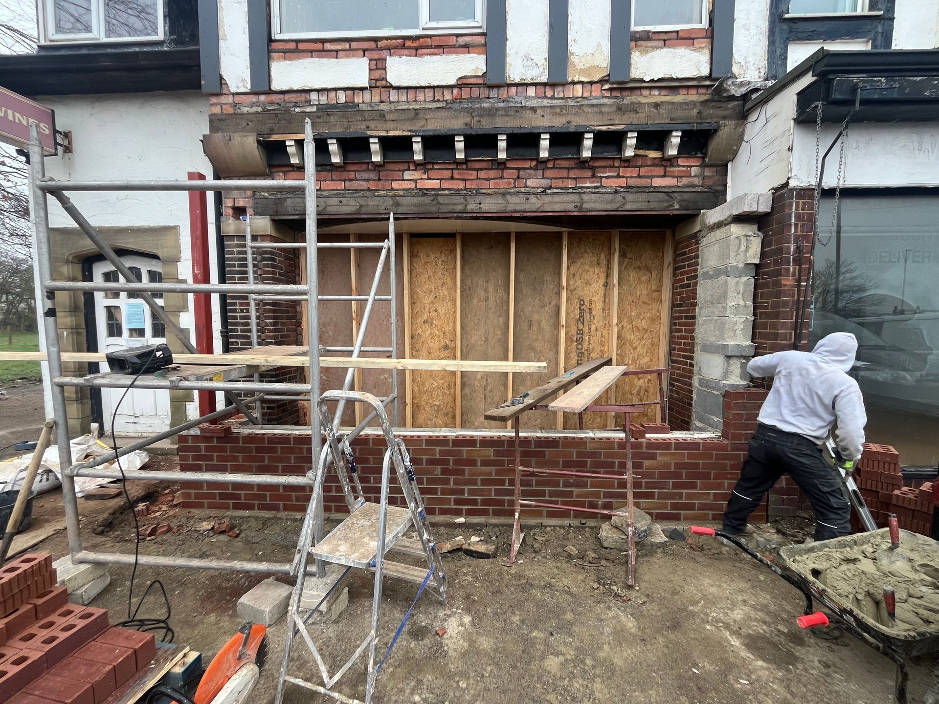 Construction worker laying bricks on a building facade. Scaffolding, tools, and materials are present.
