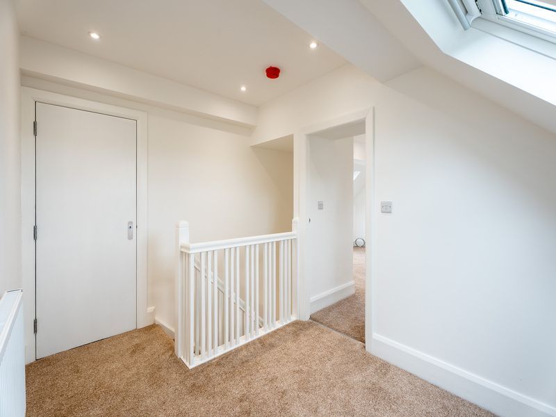 Bright hallway with carpet, white doors, and skylight. Railing separates the hallway from lower floor.