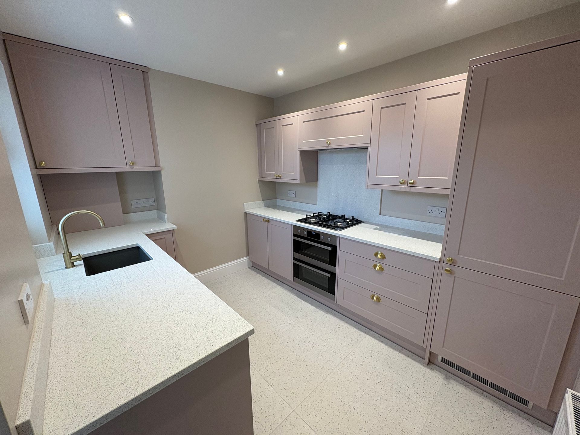 A kitchen with pale purple cabinets, white countertops, and gold hardware.