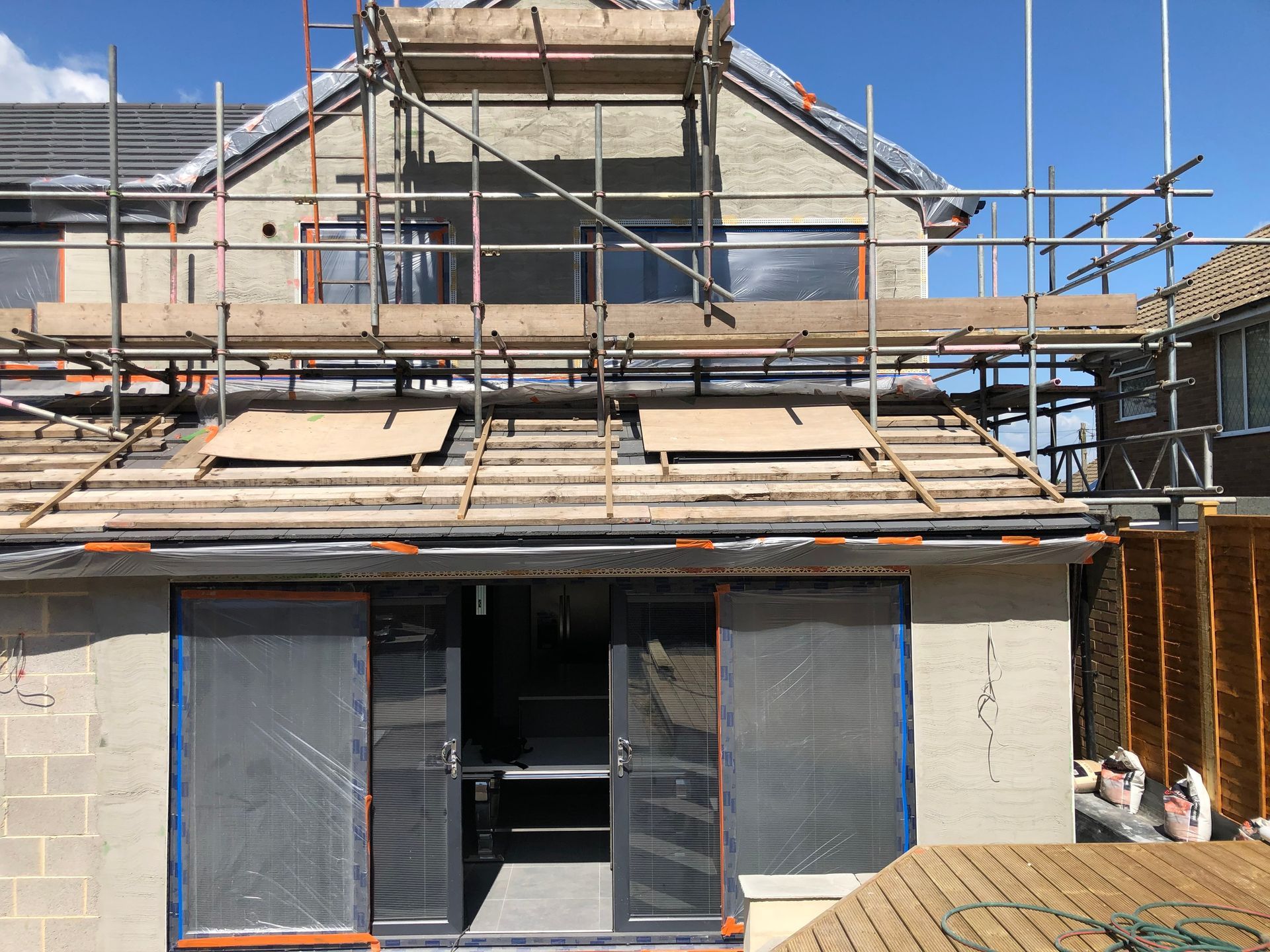 House under construction with scaffolding, featuring exposed roof and open sliding doors.