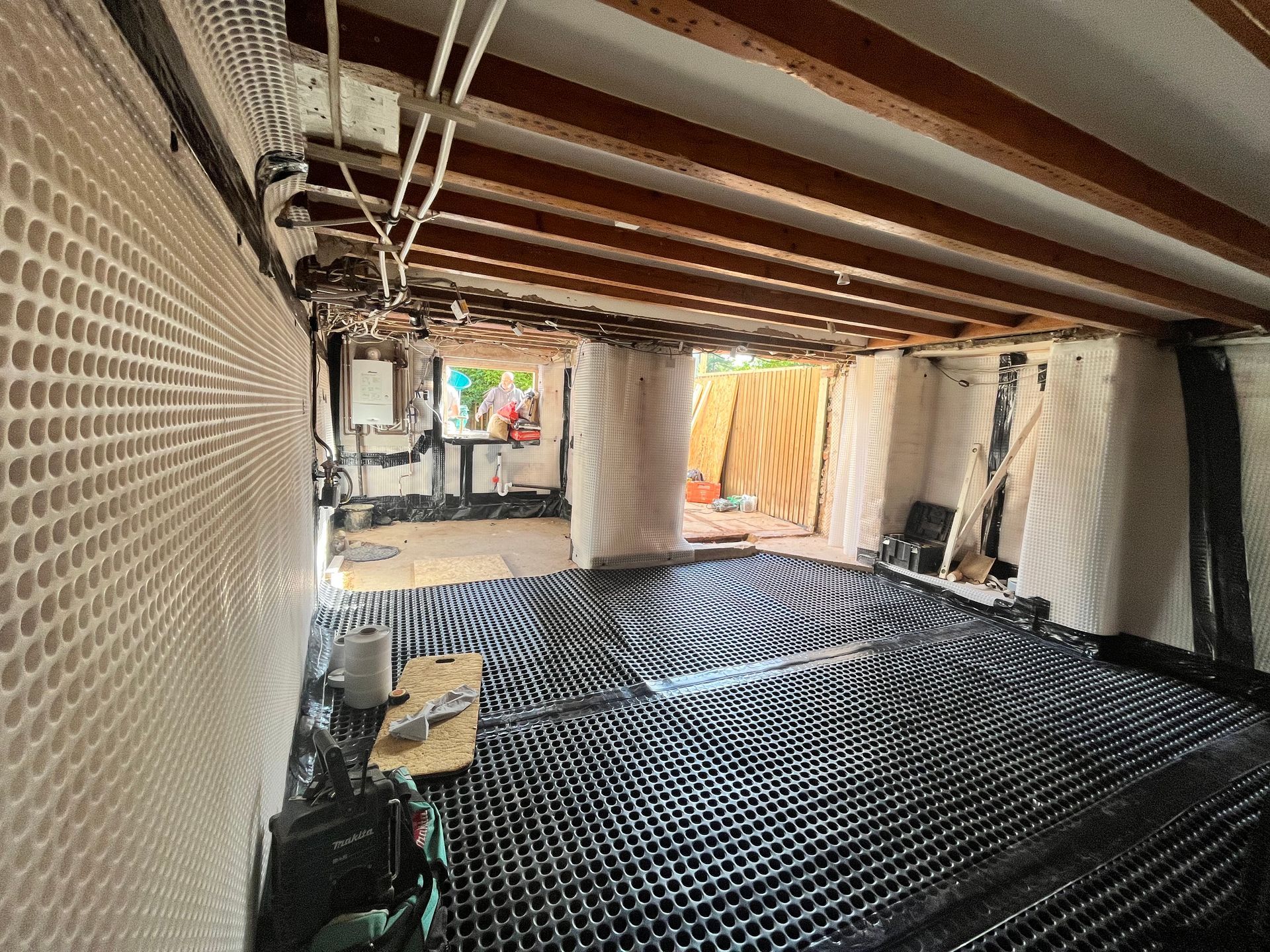 Under-construction basement with black flooring, white walls, wooden beams, and exposed pipes.
