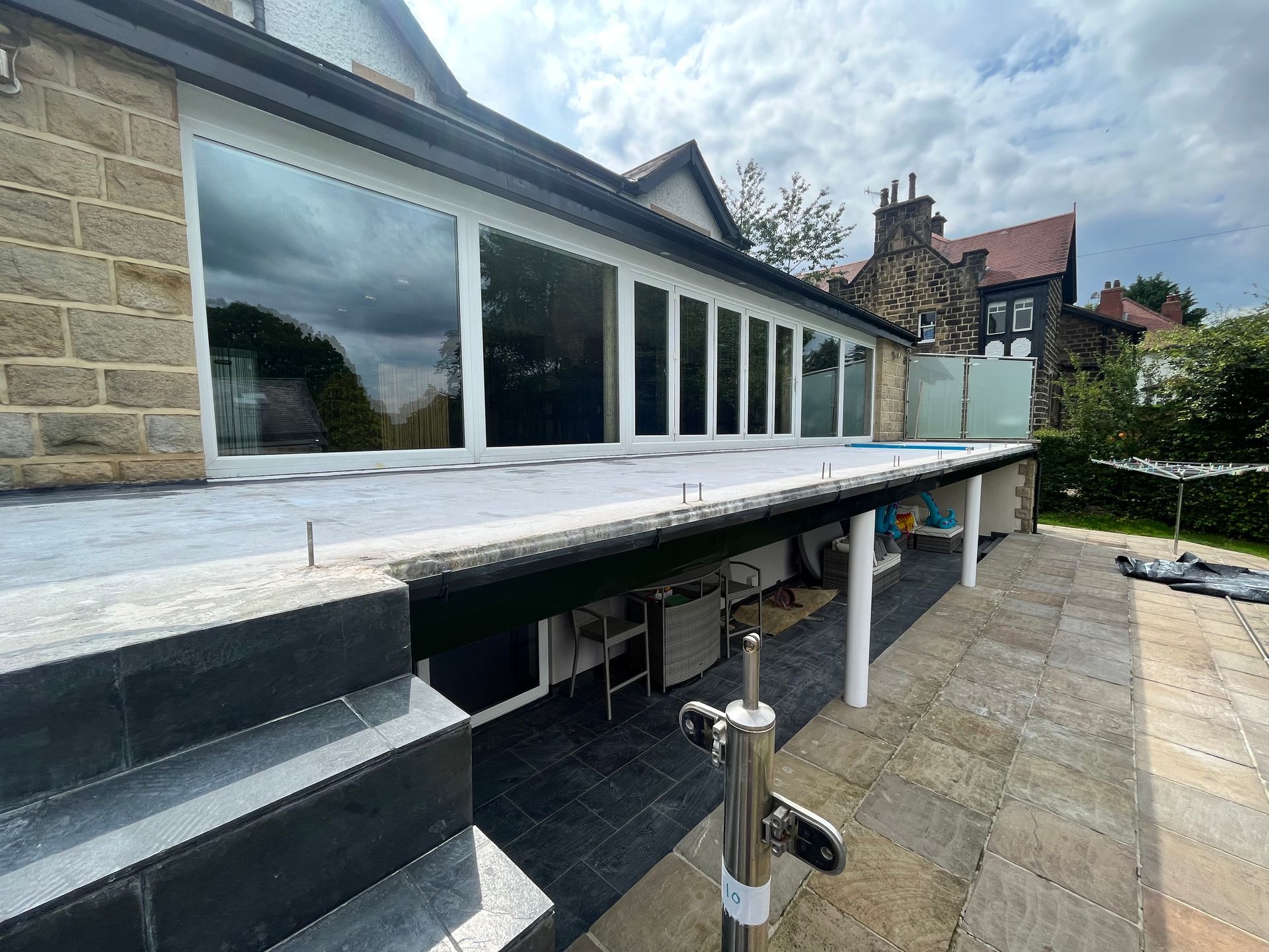A large, modern patio with bi-fold doors, stone facade, and steps leading to a lower level patio.