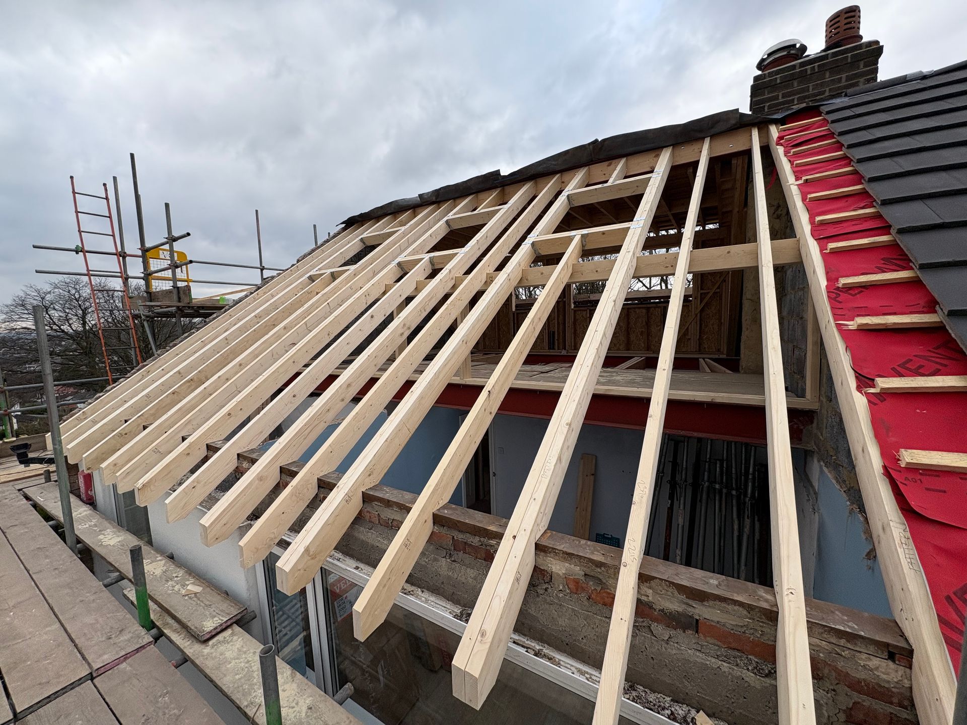Construction site: New roof rafters being installed on a brick building with a red roof edge.