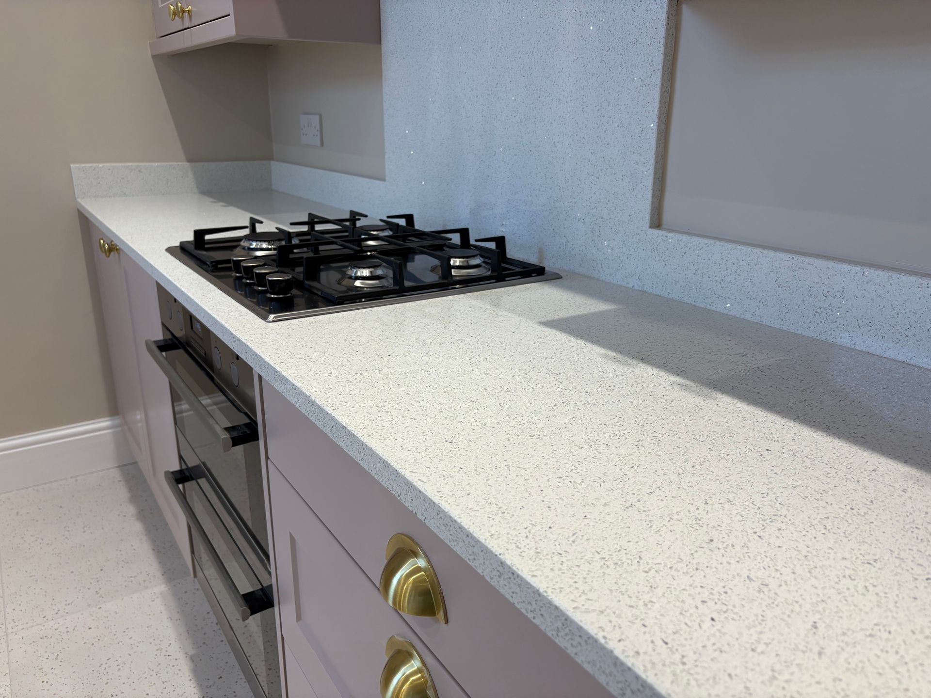 Kitchen with pale pink cabinets, white countertop, black gas stove, and built-in oven.
