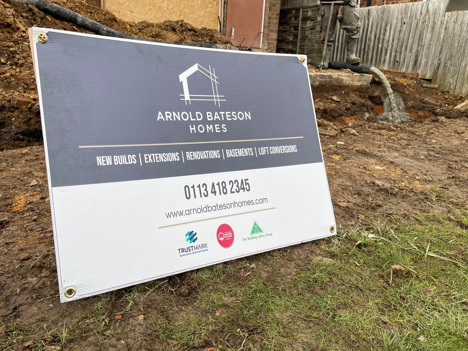 Sign for Arnold Bateson Homes at a construction site. Gray and white, logo and contact info visible.