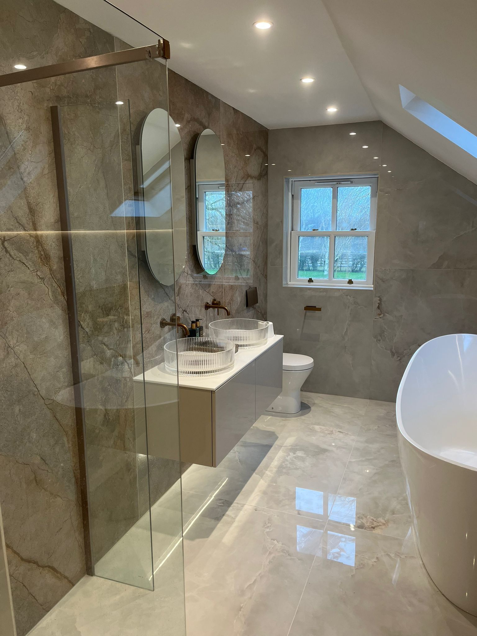 Luxurious bathroom with marble-effect walls and floor. Features a floating vanity with dual sinks, oval mirrors