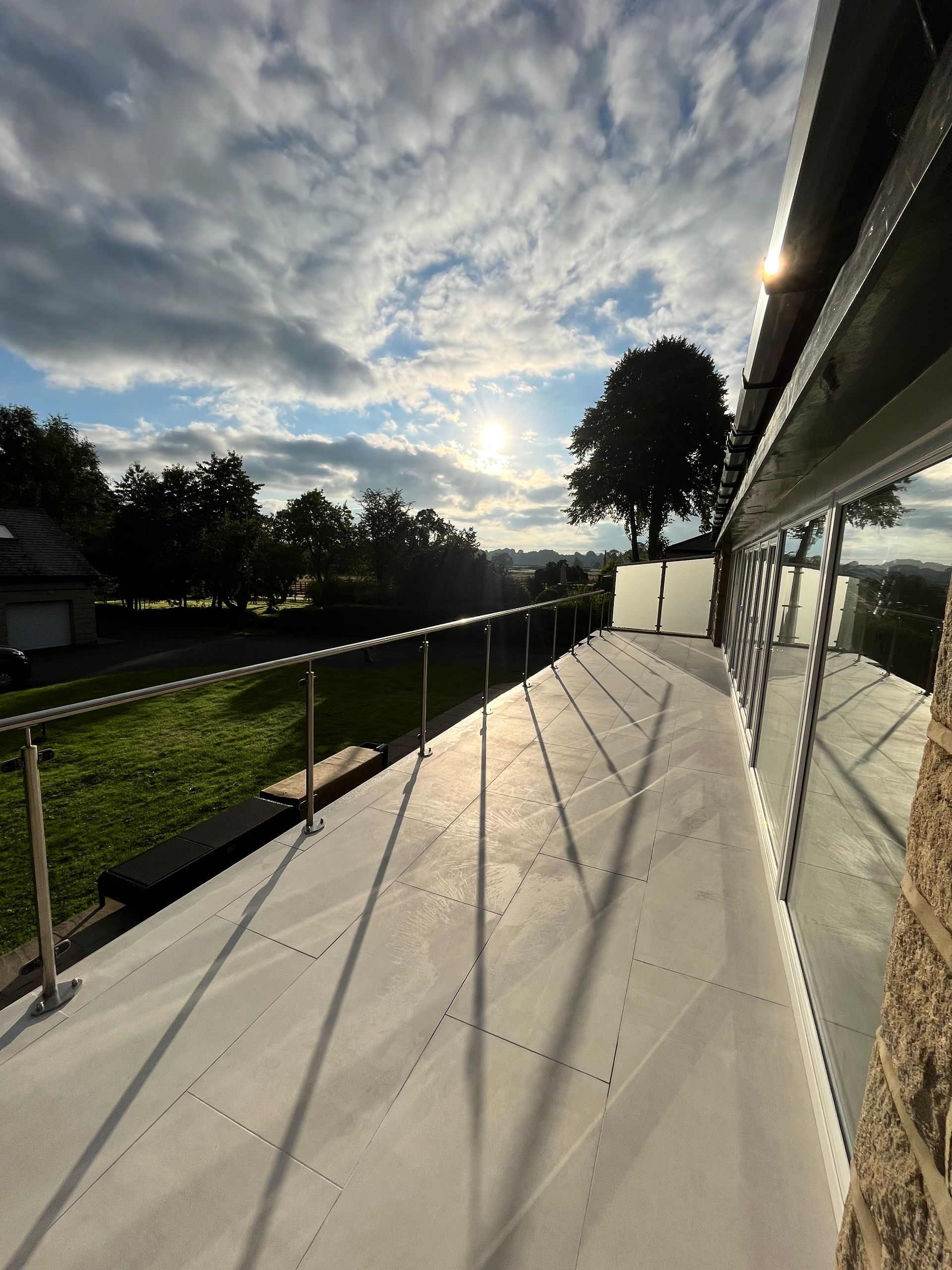 Balcony with a stainless steel railing, overlooking a green landscape under a partly cloudy sky.