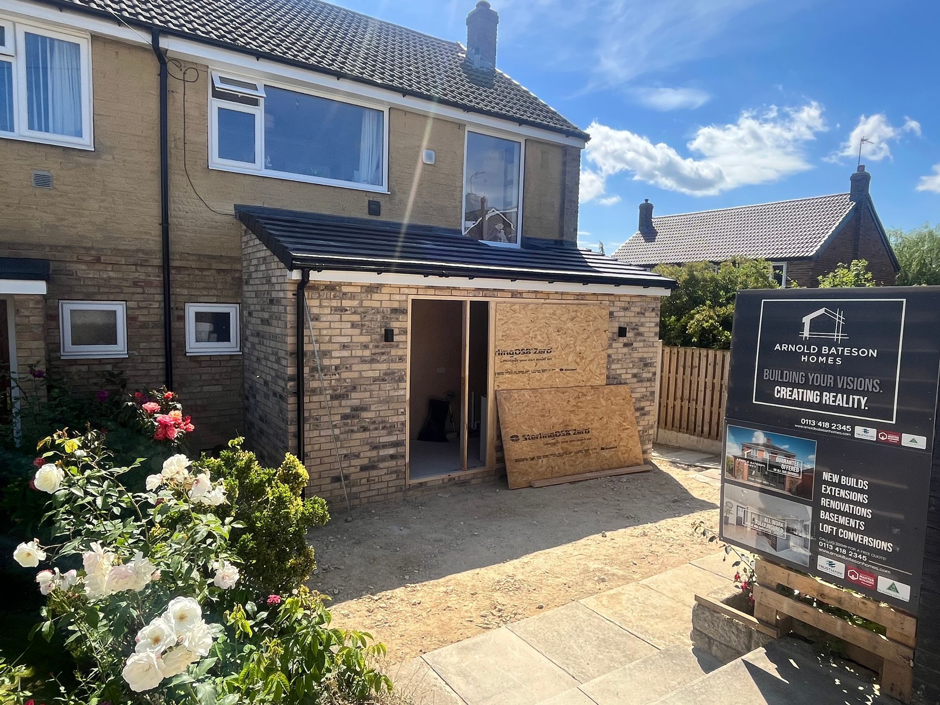 House with a new brick extension, construction site, under blue sky.