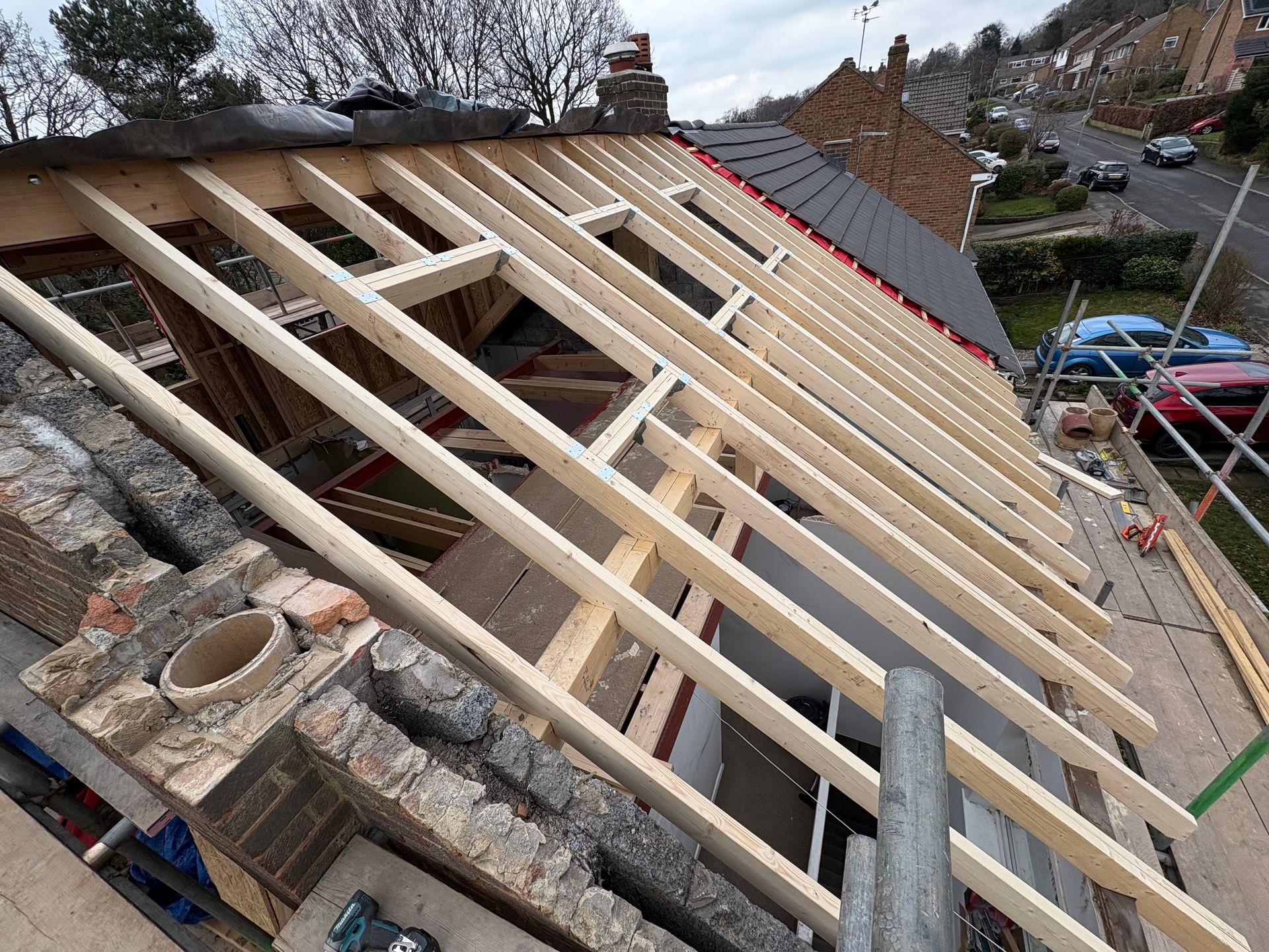 Roof construction: wooden beams laid over brick chimney, partial tiling on the roof.