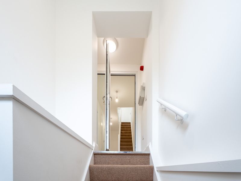 Looking up stairs into a bright, white stairwell with a glass door and an additional staircase beyond.