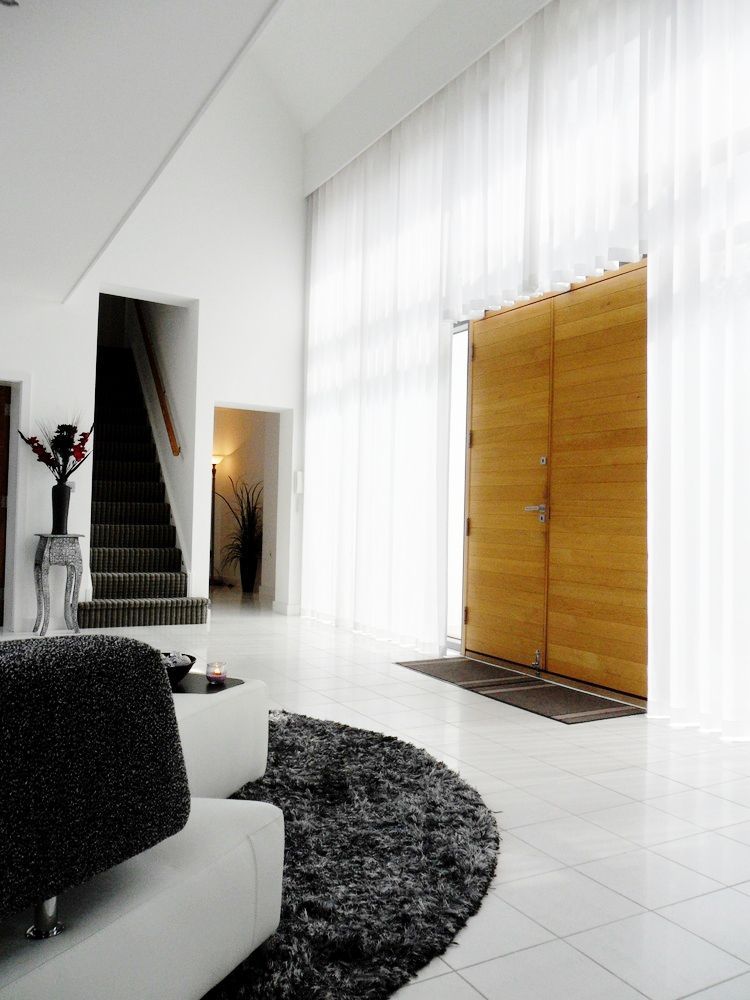 Bright entryway with large wooden doors, sheer curtains, a dark rug, and staircase.