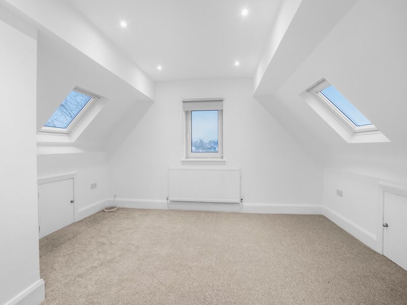 Empty, white attic room with carpet, three windows, and recessed lighting.