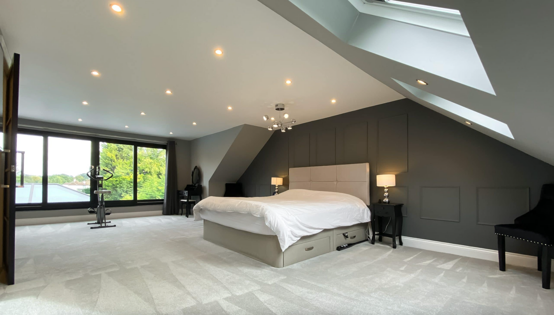 Spacious modern bedroom with gray walls, a large bed, and natural light from skylights and windows.