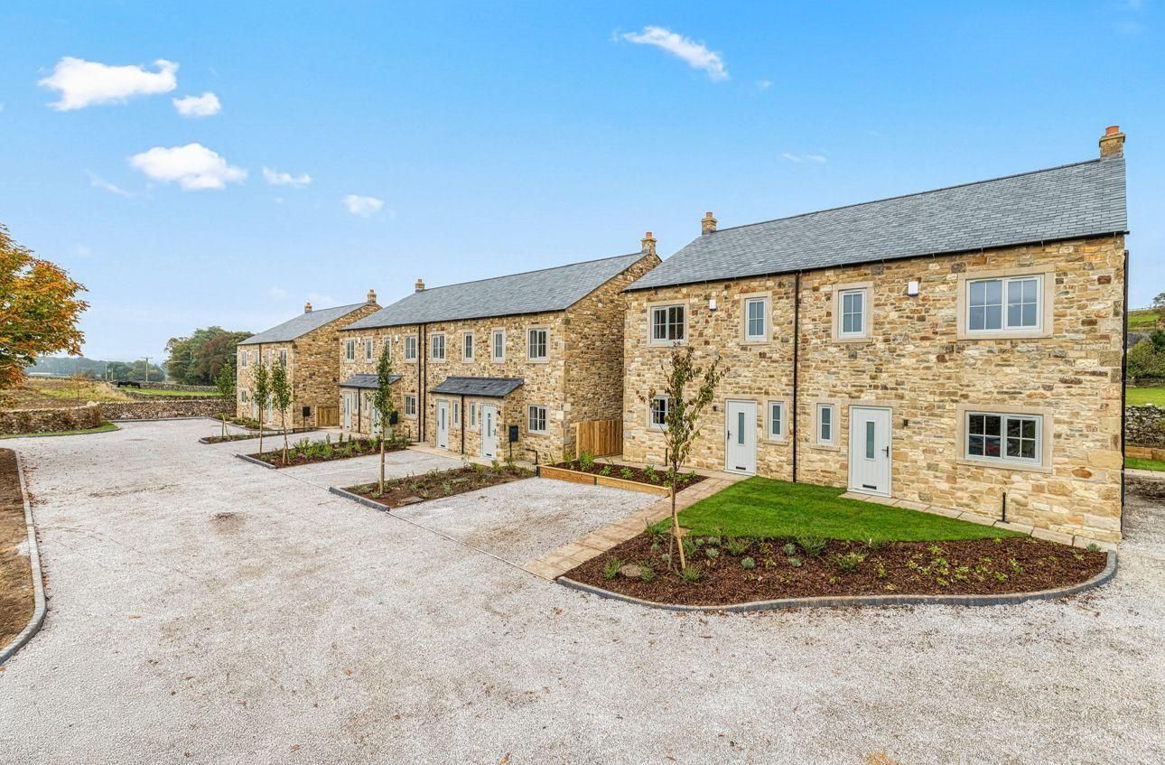 Row of stone houses with gravel driveway under a blue sky.