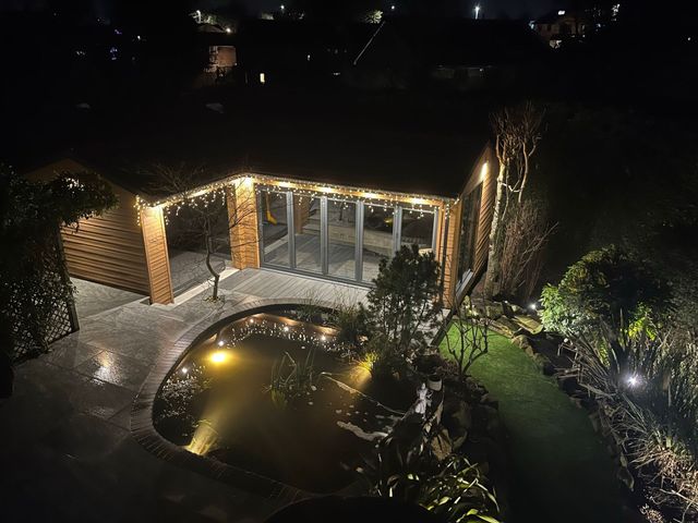 Wooden gazebo with glass doors and a pond illuminated at night.