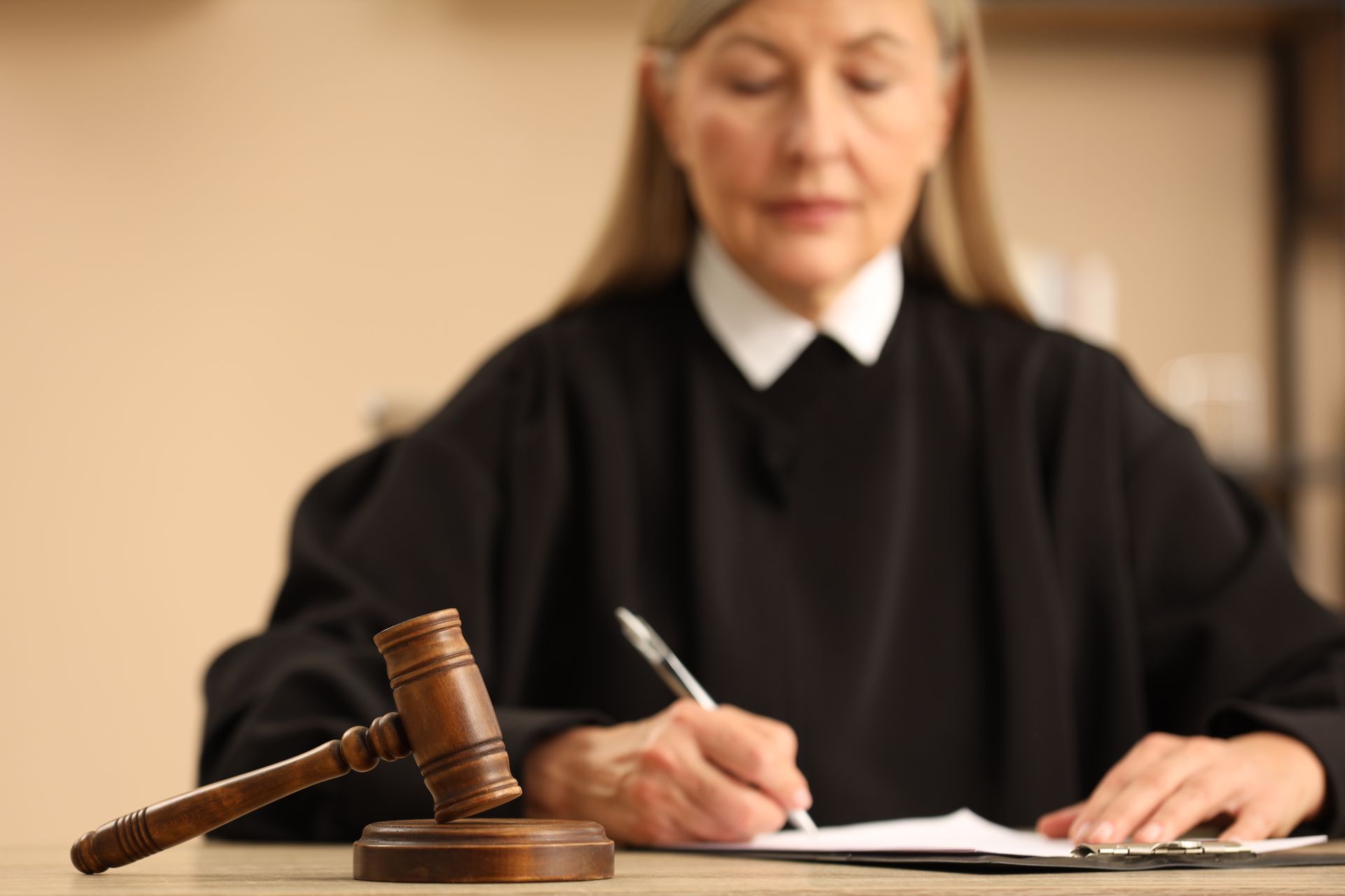 Judge in black robe, writing at desk with gavel.