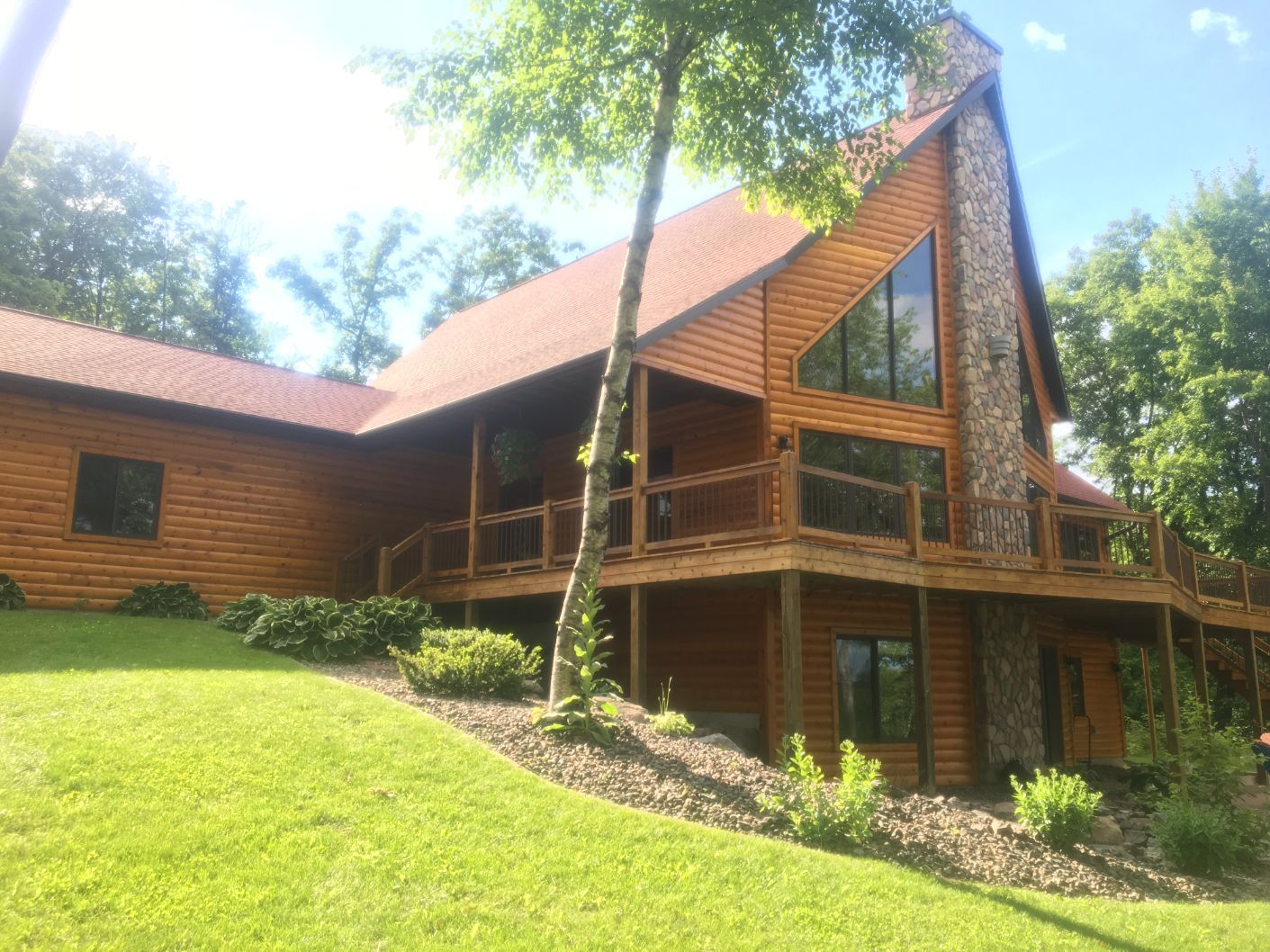Wood cabin with a stone chimney, balcony, and green lawn.