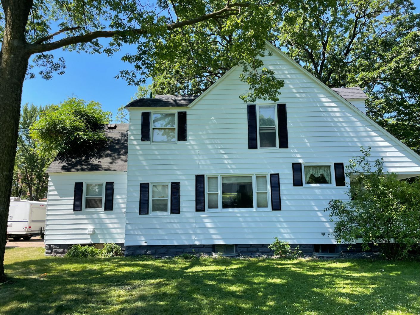 White two-story house with black shutters, trees partially obscure the building; sunny day.